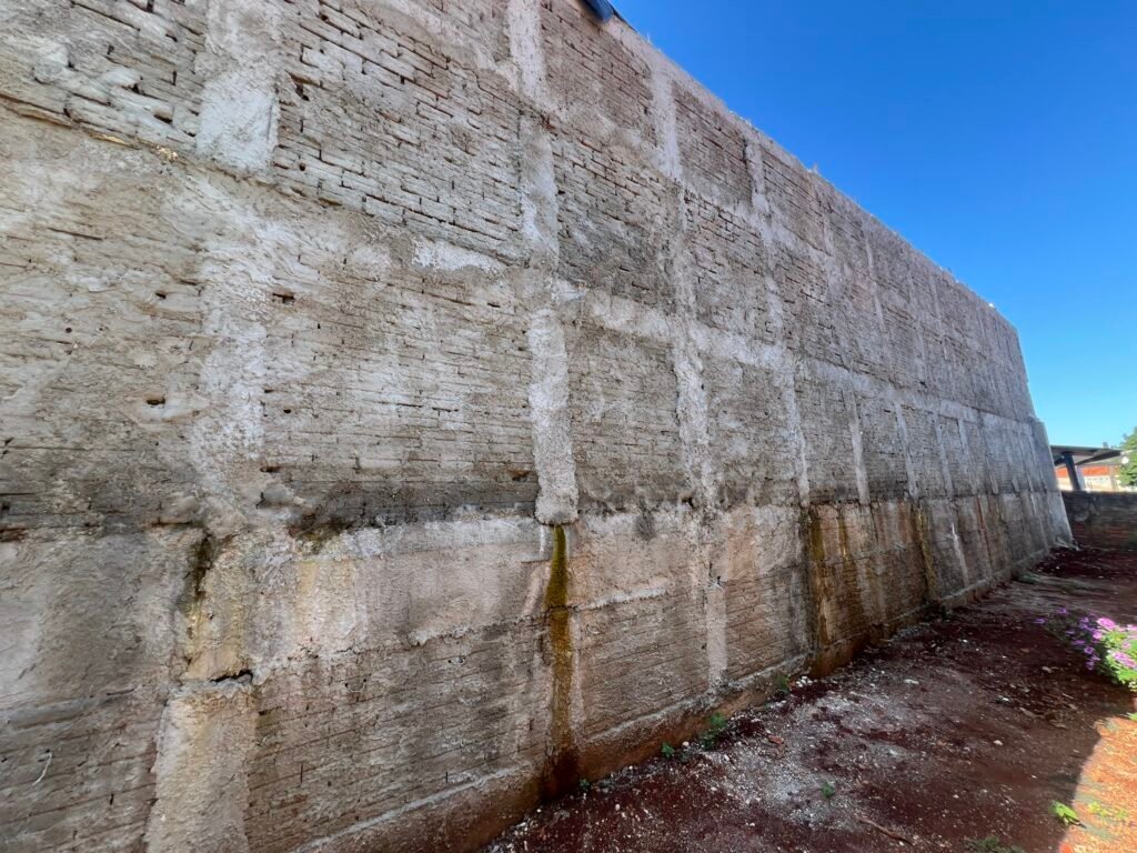 Muro de arrimo em alvenaria com manchas de umidade visíveis na base, identificado durante vistoria técnica para elaboração de laudo em Londrina.