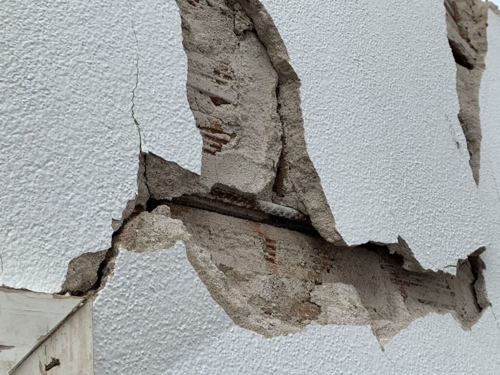 Fissuras profundas e destacamento de revestimento em parede de alvenaria vinculada ao muro de arrimo em Londrina.