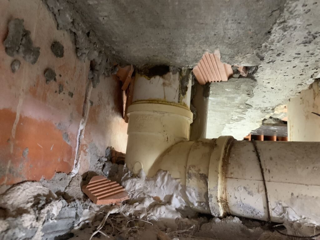 Tubulação com sinais de infiltração e má vedação sob a laje, relacionada a vazamento no teto do banheiro