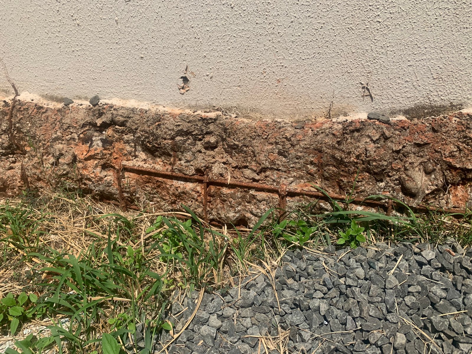 Base da parede encostada na terra, com o reboco destruído e o ferro aparecendo