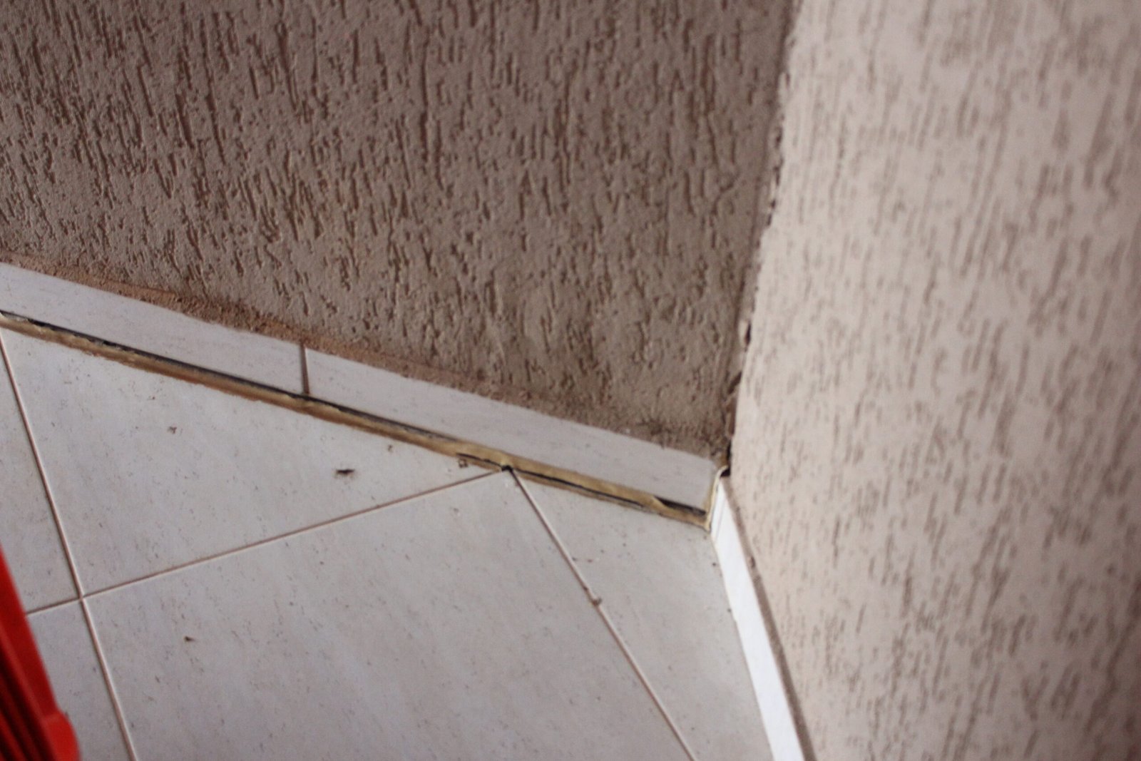 Rodapé de cerâmica soltando da parede, com fresta aberta entre o rodapé e o piso