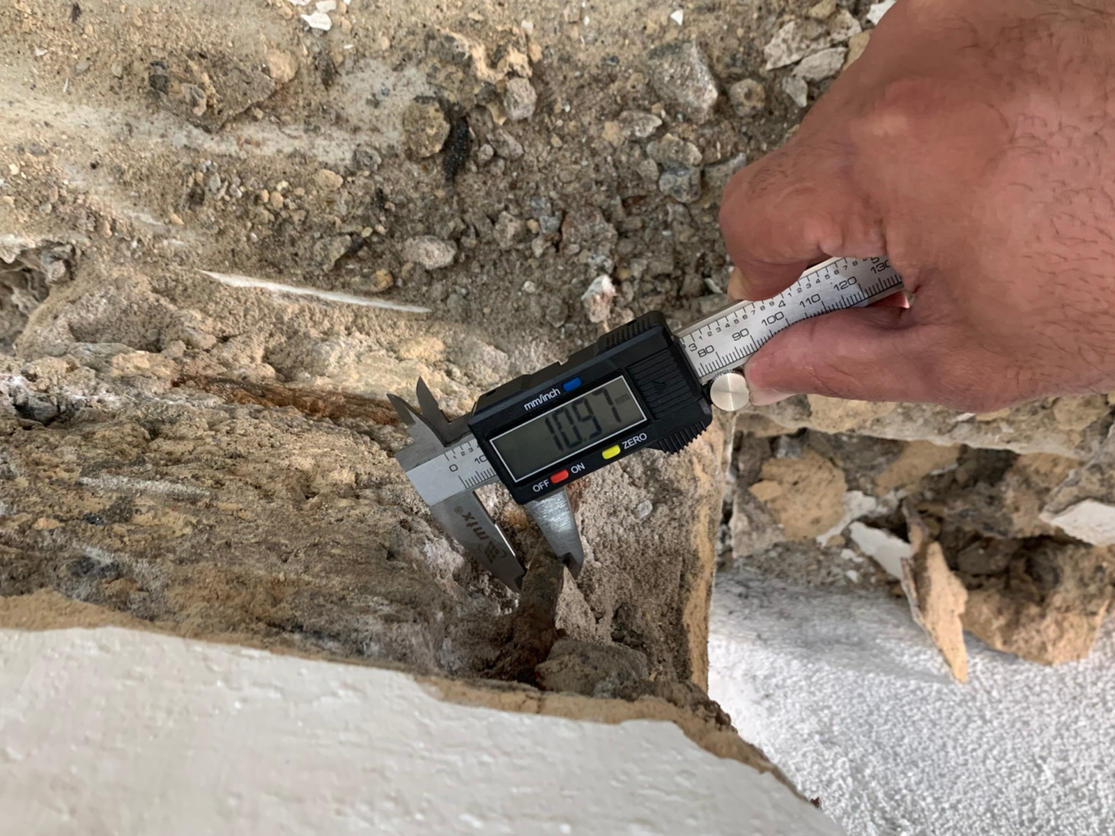 Medição com paquímetro de concreto rachado e soltando, com o ferro enferrujado aparecendo