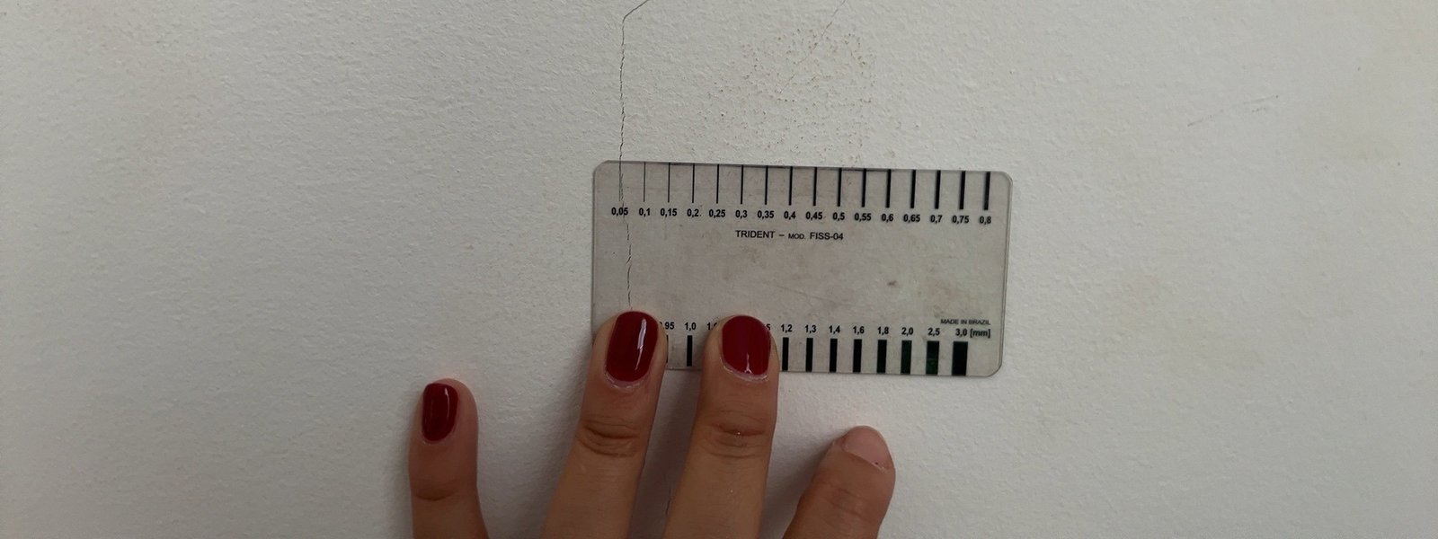 Engenheira medindo a largura da rachadura na parede com fissurômetro