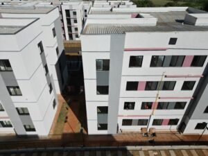 Vista aérea de dois blocos residenciais de um condomínio, mostrando fachadas brancas com faixas rosa e a passagem entre as torres.