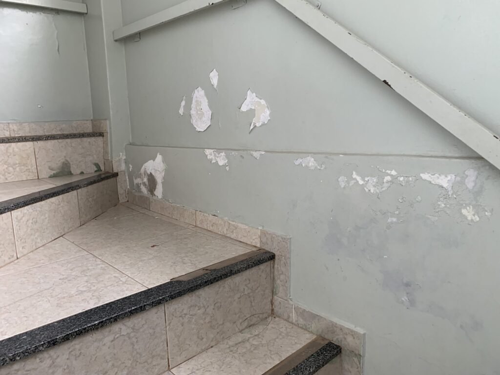 Parede de escada com revestimento descascando por umidade em vistoria técnica